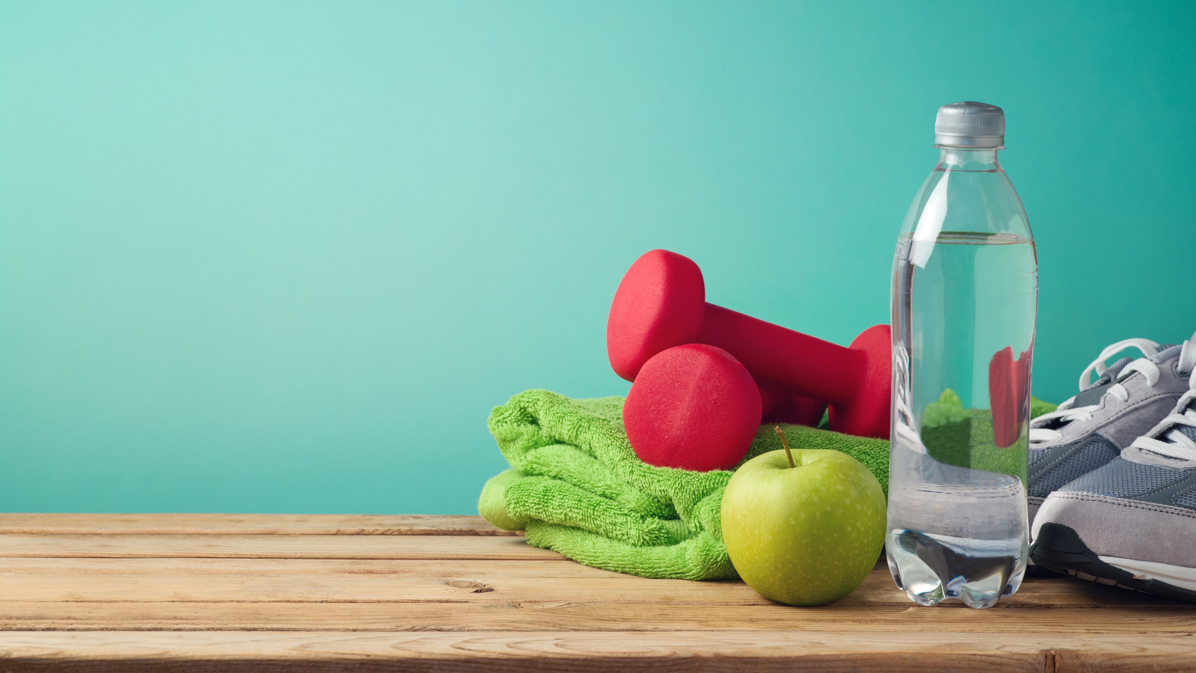 Dumbbells, a folded towel, an apple and a water bottle on a wooden bench.